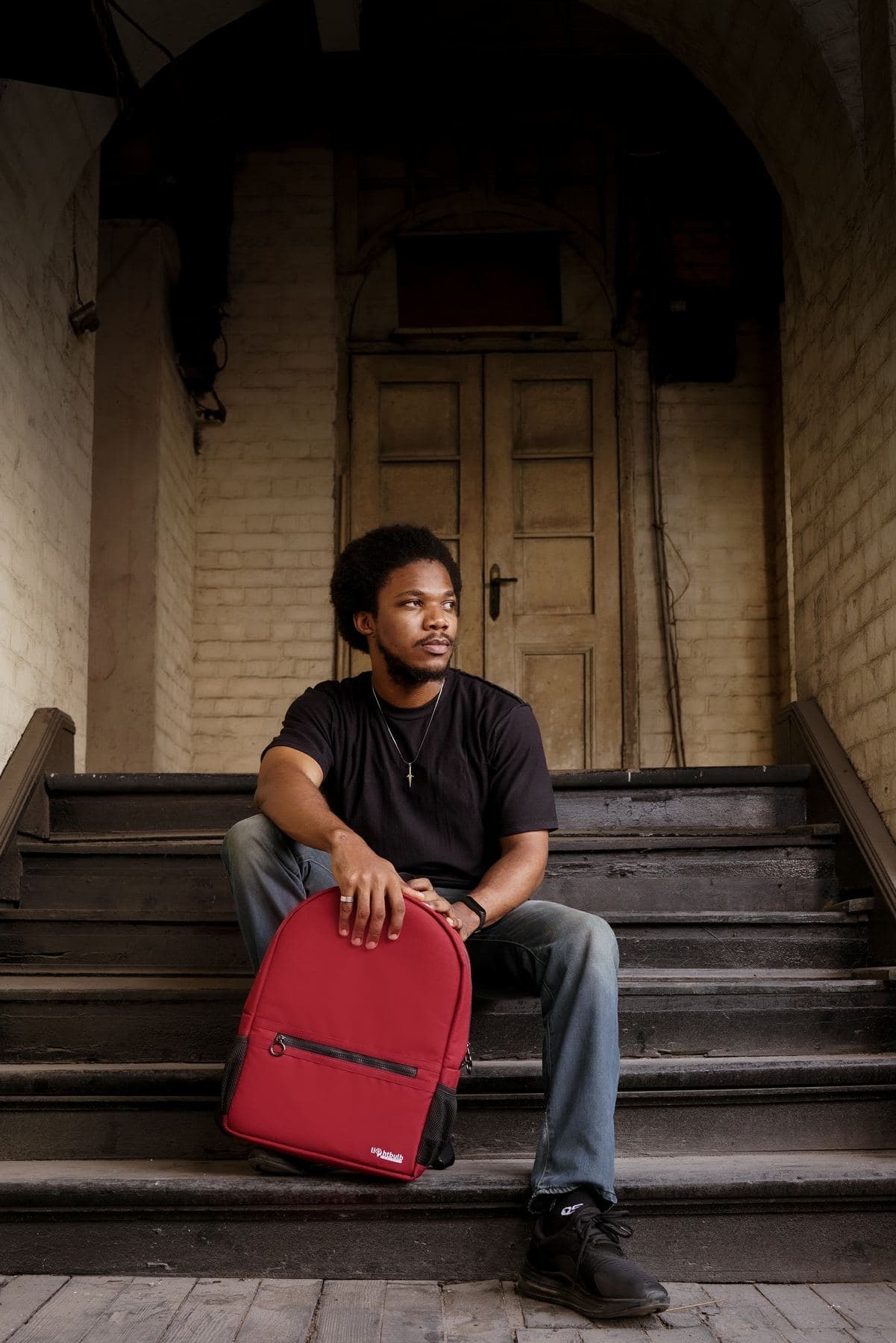 Man seated on steps with a crimson Lightbulb backpack