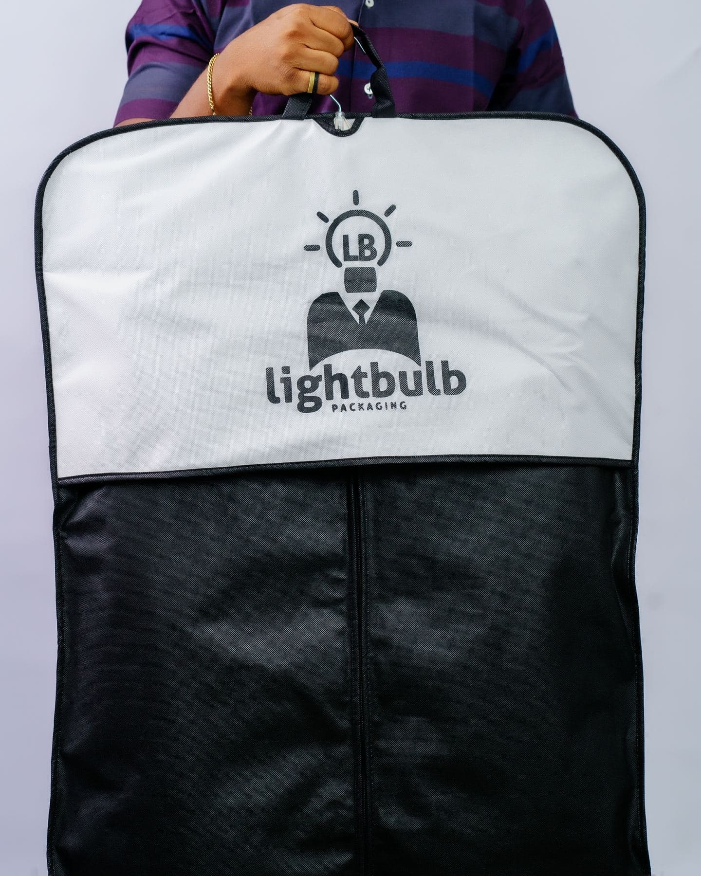 A white and black branded garment bag held up to camera