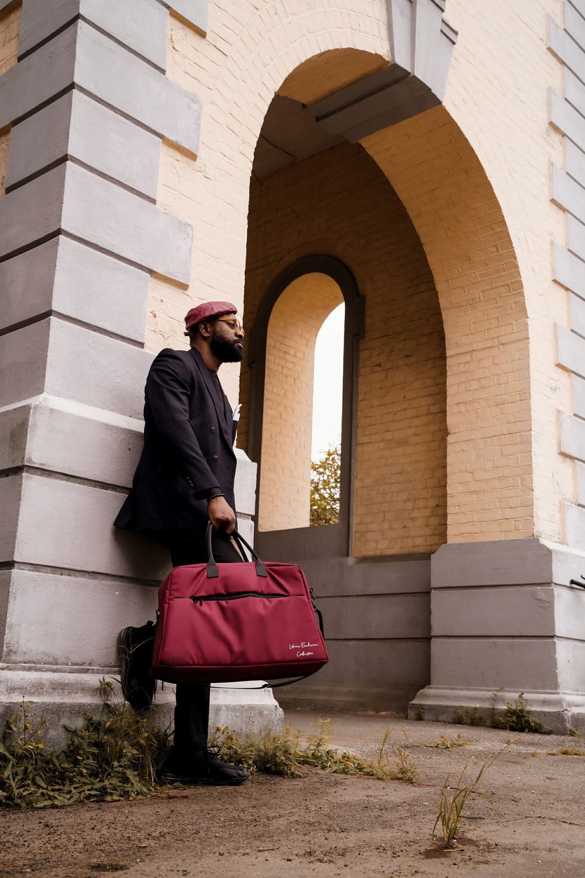 Man leaning against a stone arch holding a crimson Lightbulb weekender